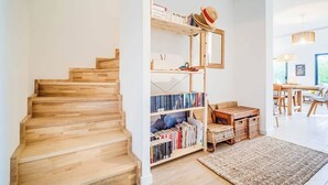 A wooden staircase leading to a living area with a bookshelf, a woven rug, and a dining area with a table and chairs. - Belle maison moderne proche plages & bourg (Carnac)