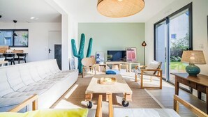 A modern living room with a white sofa, a wooden coffee table, and a television. There are two large cacti and a lamp on a side table. - Belle maison moderne proche plages & bourg (Carnac)