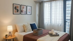 Een hotelkamer met een bed, nachtkastje met lamp, een plantje en een raam met gordijnen.