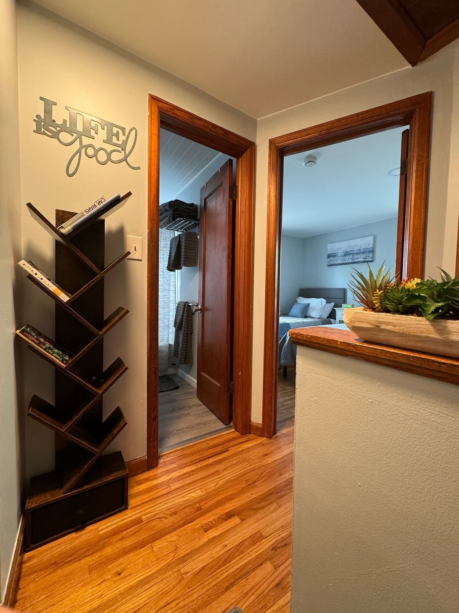 Un couloir avec un plancher en bois, une bibliothèque remplie de livres et une porte qui donne sur une chambre à coucher.