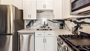 Une cuisine moderne avec des meubles blancs, un réfrigérateur en acier inoxydable, un lave-vaisselle, une cuisinière et un four à micro-ondes.
