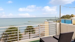 Un balcon avec vue sur la mer, un palmier et une chaise.