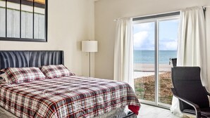 Une chambre d’hôtel avec un lit, une chaise, une lampe et une vue sur la mer, visible à travers une grande fenêtre.
