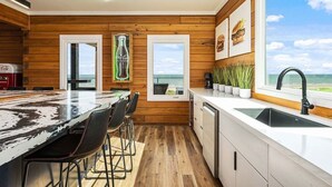 Eine moderne Küche mit Holzvertäfelung, einer großen Kochinsel mit Barhocker, Meerblick und einer Coca-Cola-Dekoration.
