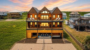 Ein zweistöckiges Holzhaus mit Balkon, Kiesauffahrt und Blick auf die Umgebung.