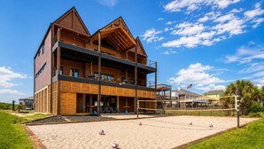 Ein zweistöckiges Holzgebäude mit Balkon, einem Sandvolleyballplatz und einer Rasenfläche.