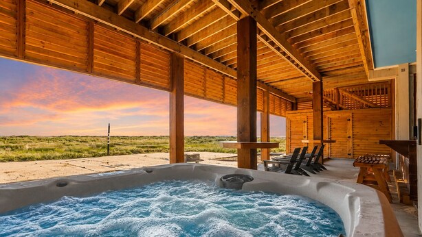 Ein Holz-Wellnessbereich mit Whirlpool, Liegestühlen und Blick auf den Strand.