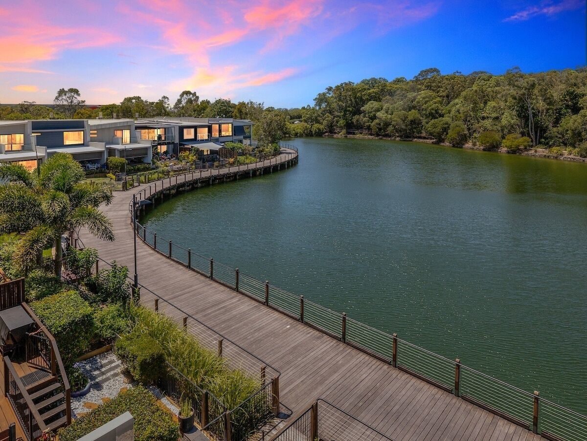 A waterfront property with a wooden deck, modern buildings, and lush greenery.