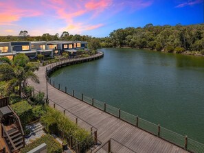 A waterfront property with a wooden deck, modern buildings, and lush greenery. - Lakefront Lux-3 Levels-Sauna, Cold Plunge & Pool (Maroochydore)
