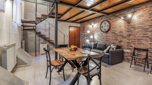 Un salon moderne avec une table à manger en bois, des chaises, un canapé et un mur en briques.