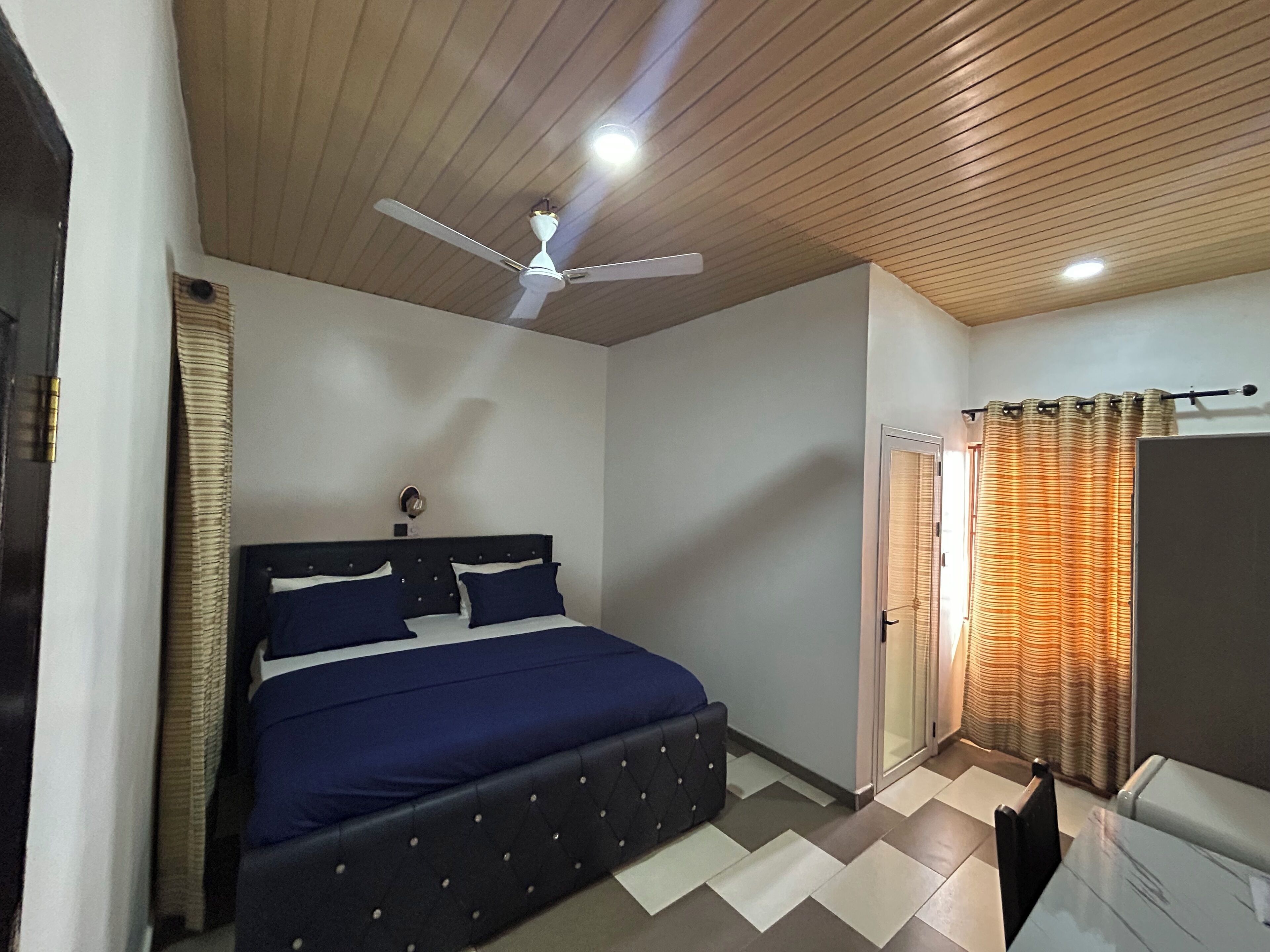 Un dormitorio con cama, ventilador de techo, ventana con cortinas y puerta.