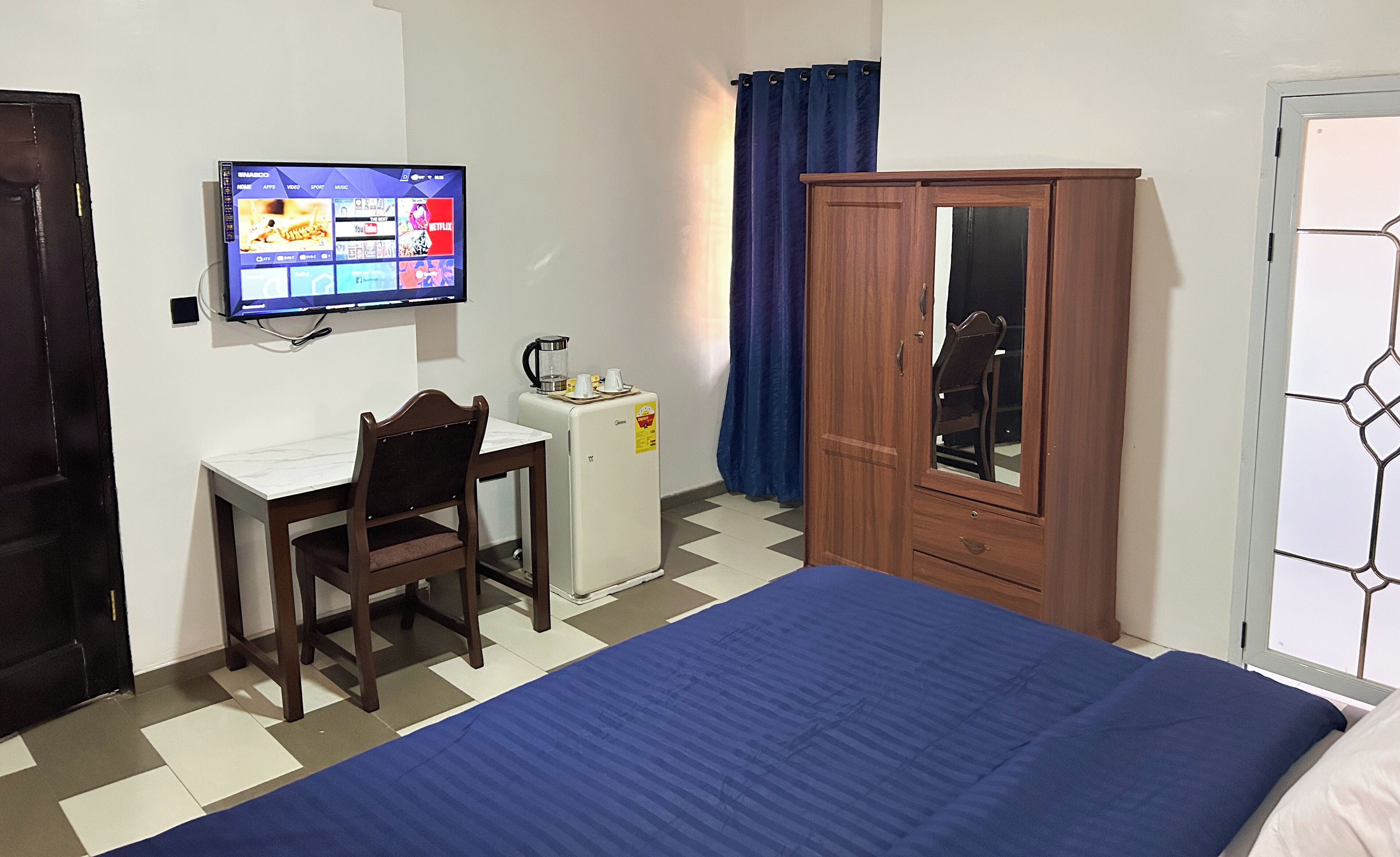 A hotel room with a bed, a desk with a chair, a television, a wardrobe, and a coffee maker.