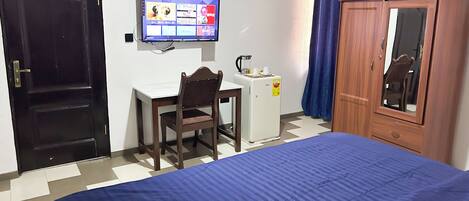 A bedroom with a bed, a desk with a chair, a television, a wardrobe, and a small refrigerator.