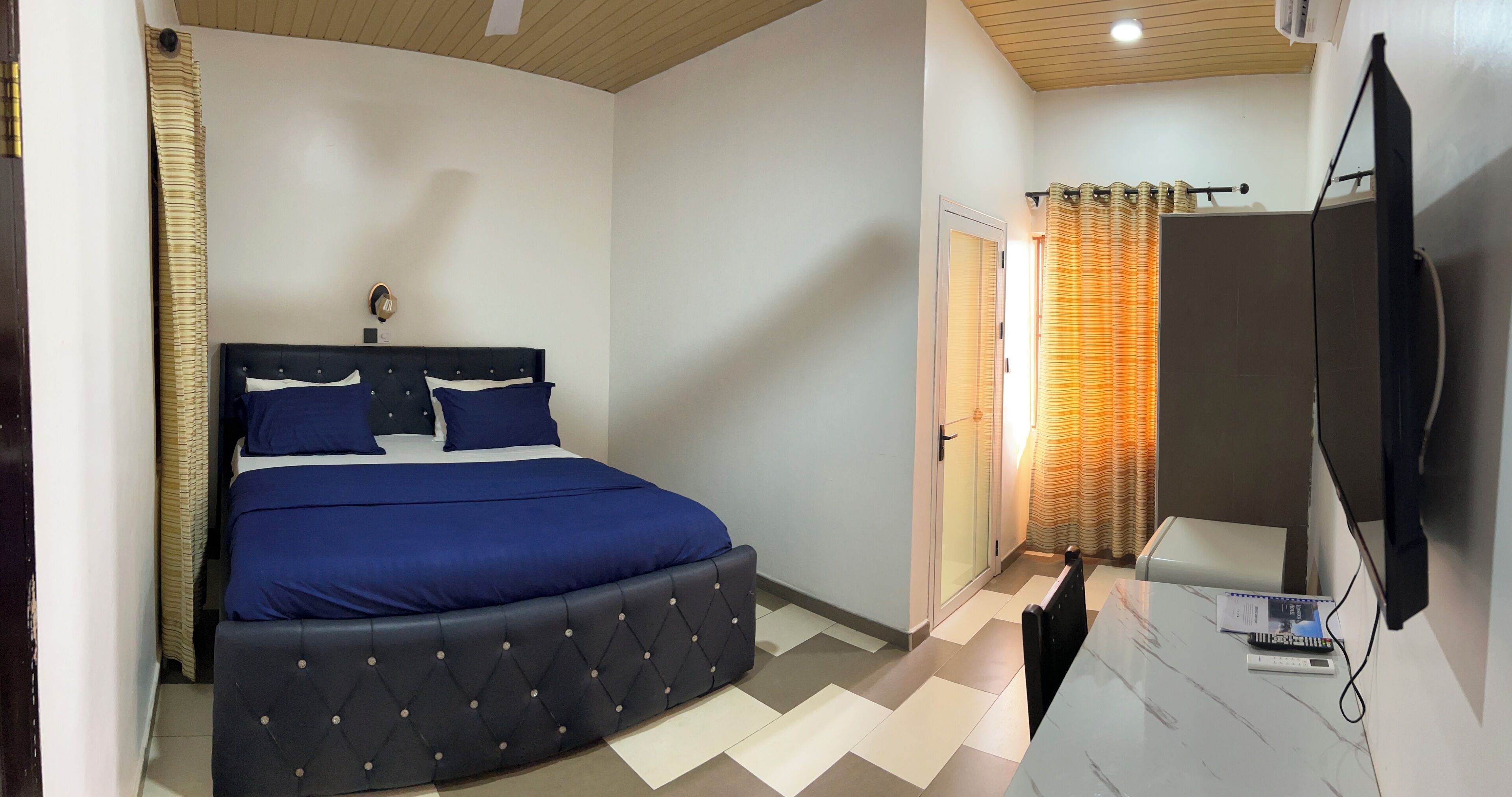 A bedroom with a bed, a TV, and a bathroom with a shower curtain.