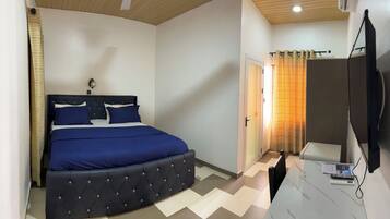A bedroom with a bed, a TV, and a bathroom with a shower curtain.