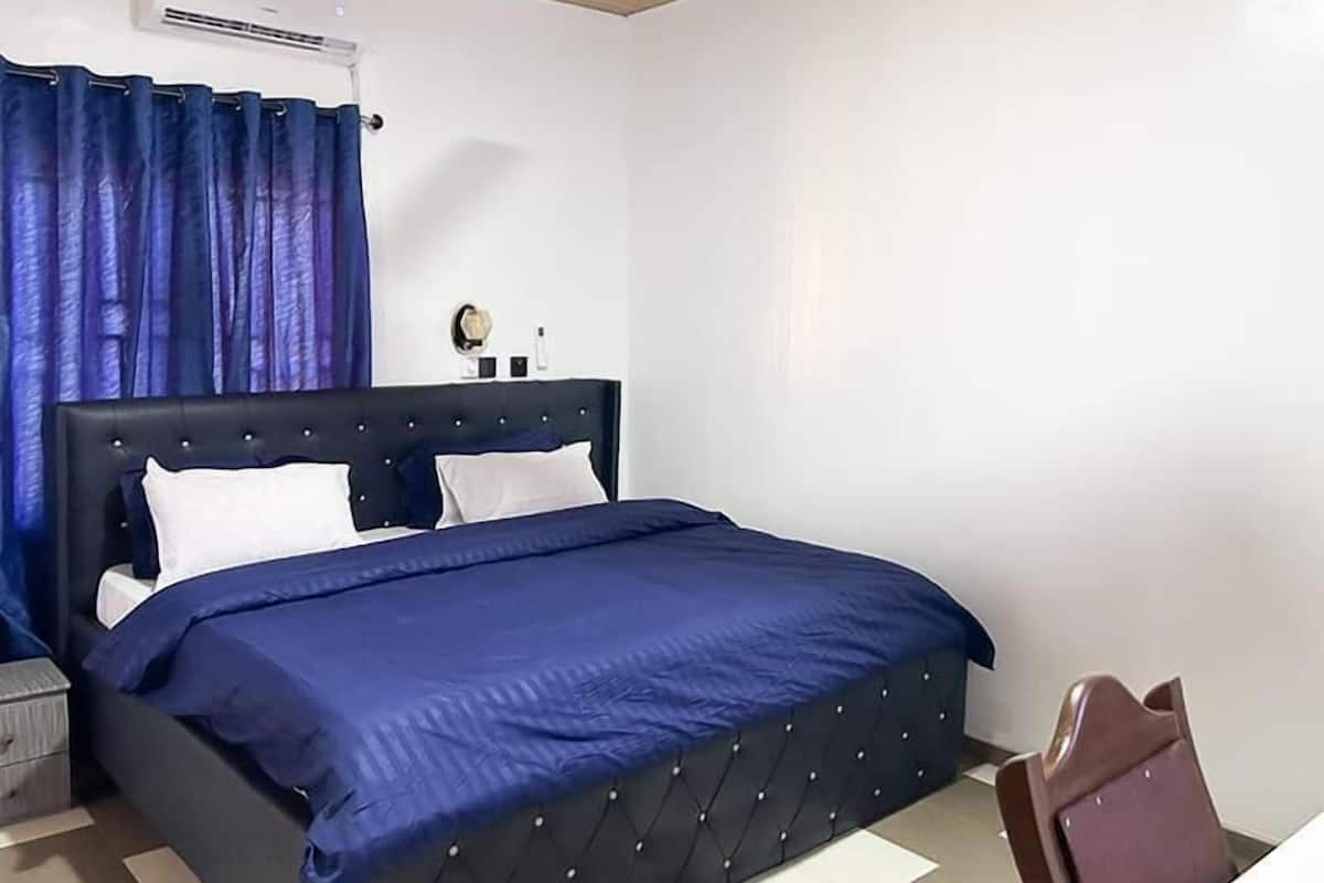 A bedroom with a large bed, a nightstand, a chair, and a wall-mounted air conditioner.