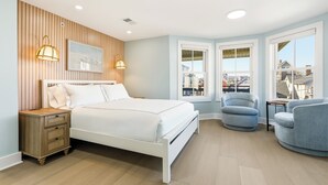 A bedroom with a bed, bedside table, two chairs, and a window with a view. - The Marilyn Inn (Ocean Grove)