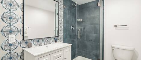 Une salle de bain avec une douche à parois de verre, un lavabo blanc et des toilettes.