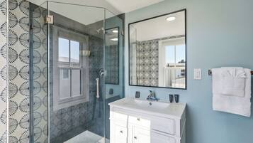 Une salle de bain dotée d’une douche à parois de verre, d’un meuble-lavabo blanc avec un miroir et de carreaux muraux à motifs.