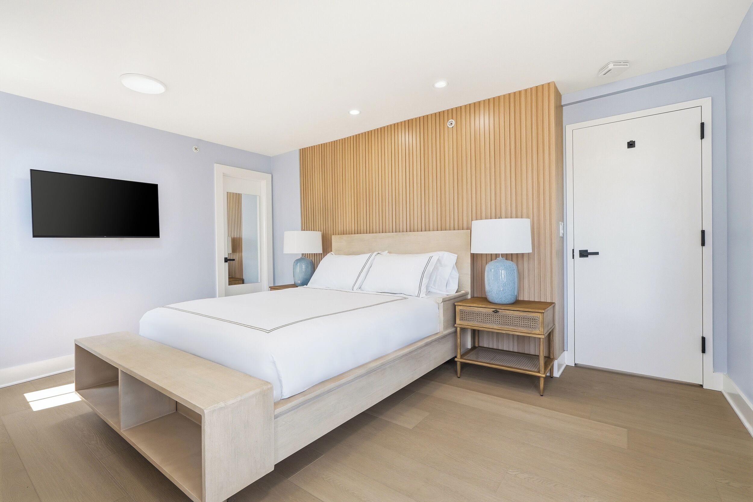 A modern bedroom with a bed, bedside tables, a TV, and a door.