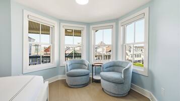 Una habitación de esquina con ventanas amplias, una cama blanca, dos sillones azules y una pequeña mesa.