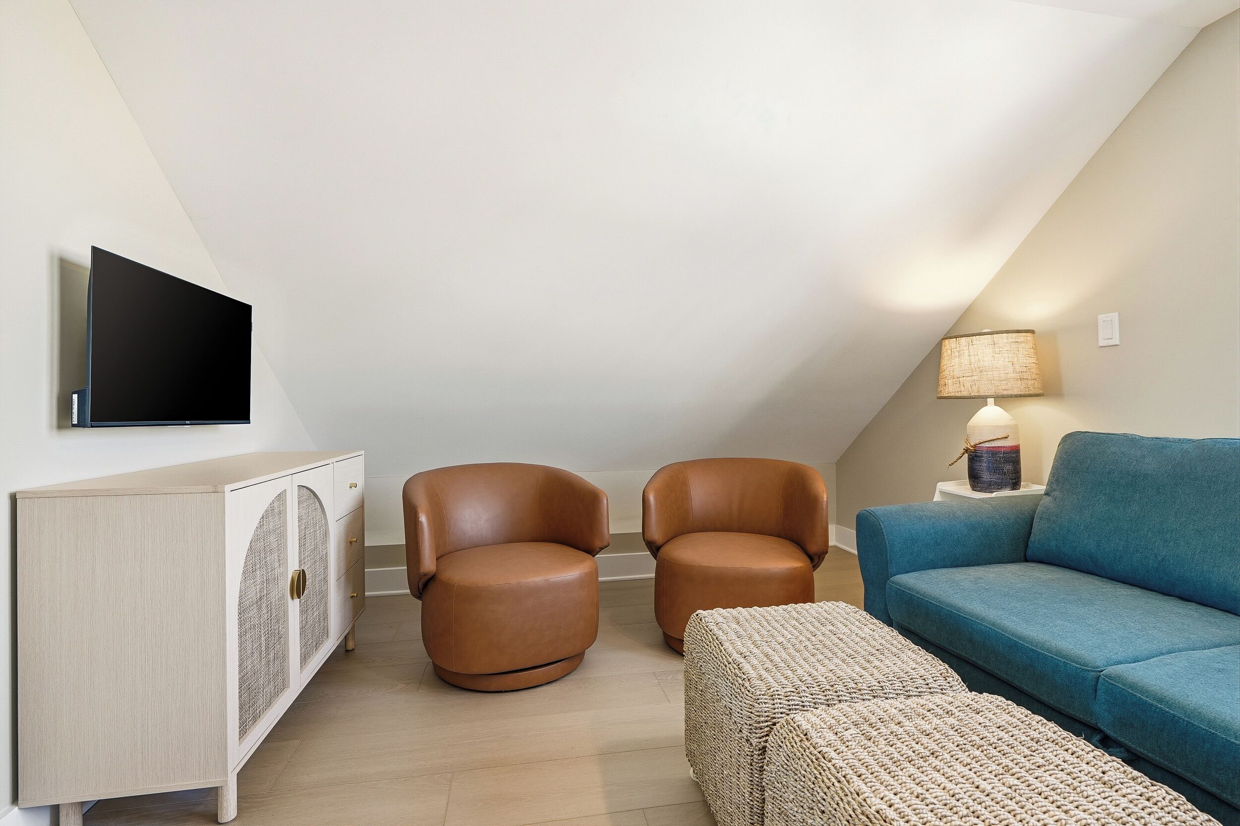 Una sala de estar moderna con un sofá, dos sillones, un televisor montado en un mueble bajo y una lámpara sobre una mesita.
