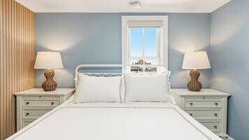 A bedroom with a bed, two bedside tables, a window, and a view of buildings.