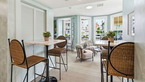A dining area with wicker chairs, a wooden table, and potted plants. - The Marilyn Inn (Ocean Grove)
