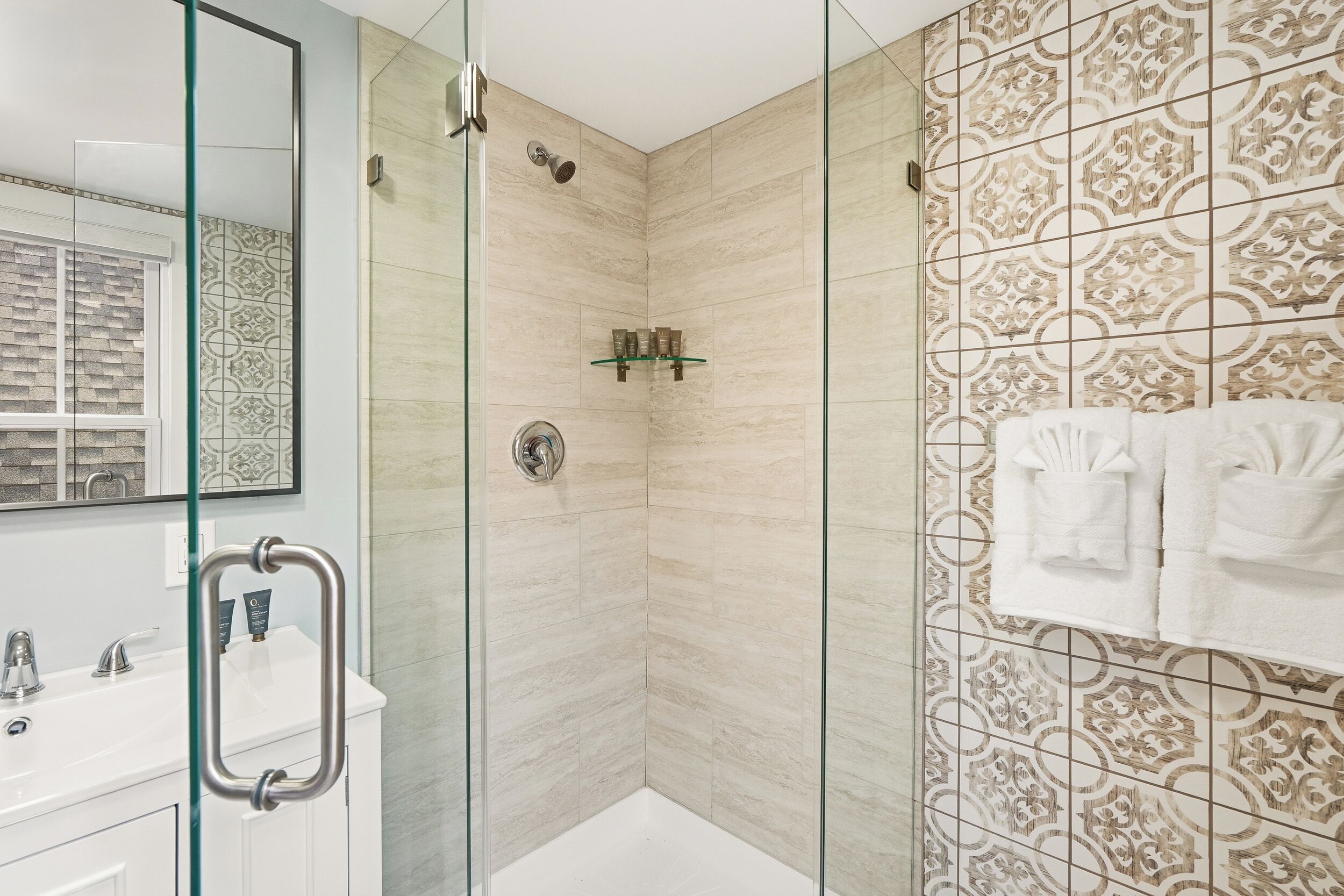 A modern bathroom with a glass shower enclosure, a white sink, and patterned tiles.