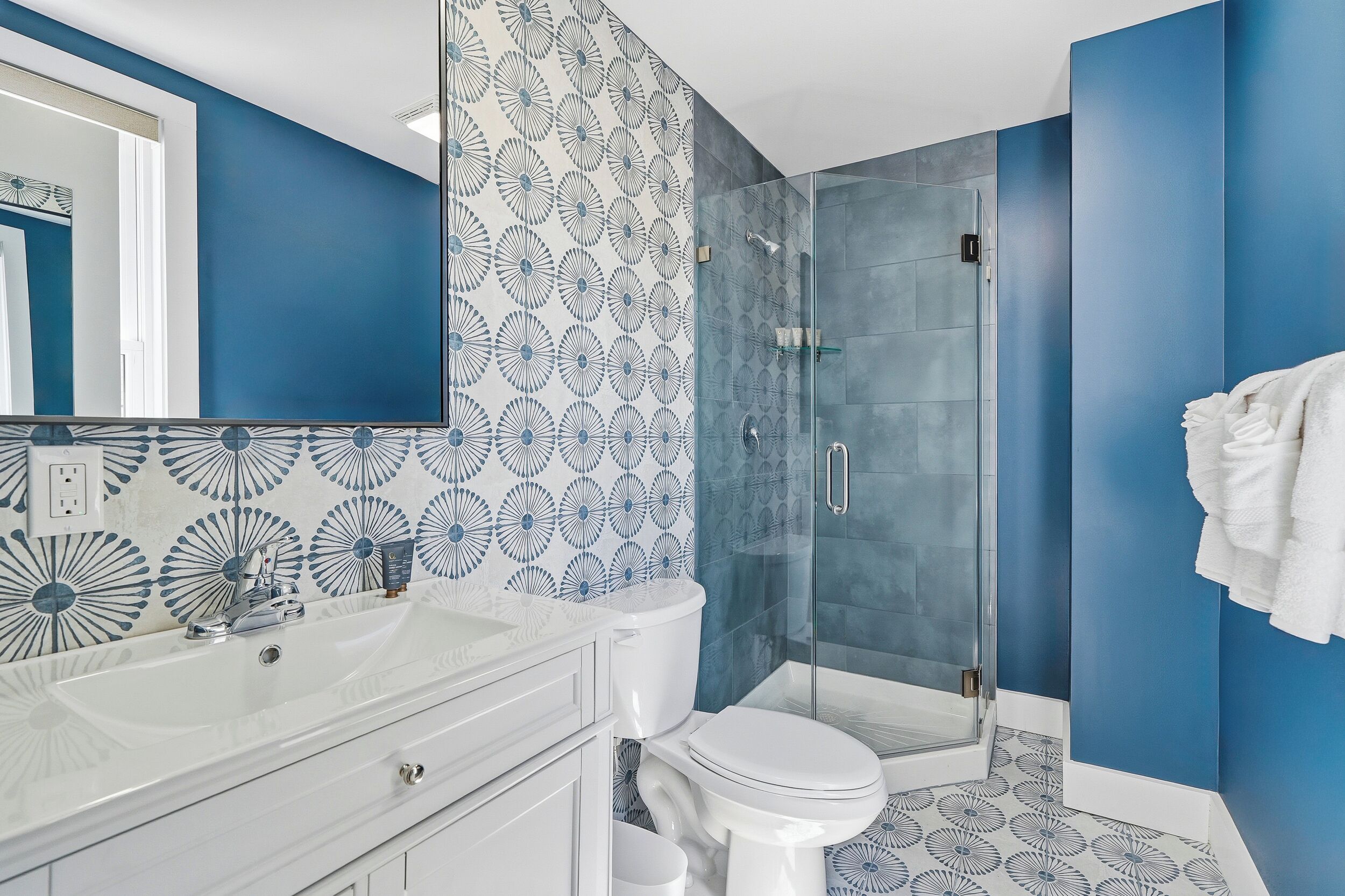 Un baño moderno con un espejo grande, un lavabo blanco, inodoro y ducha envuelta en vidrio.