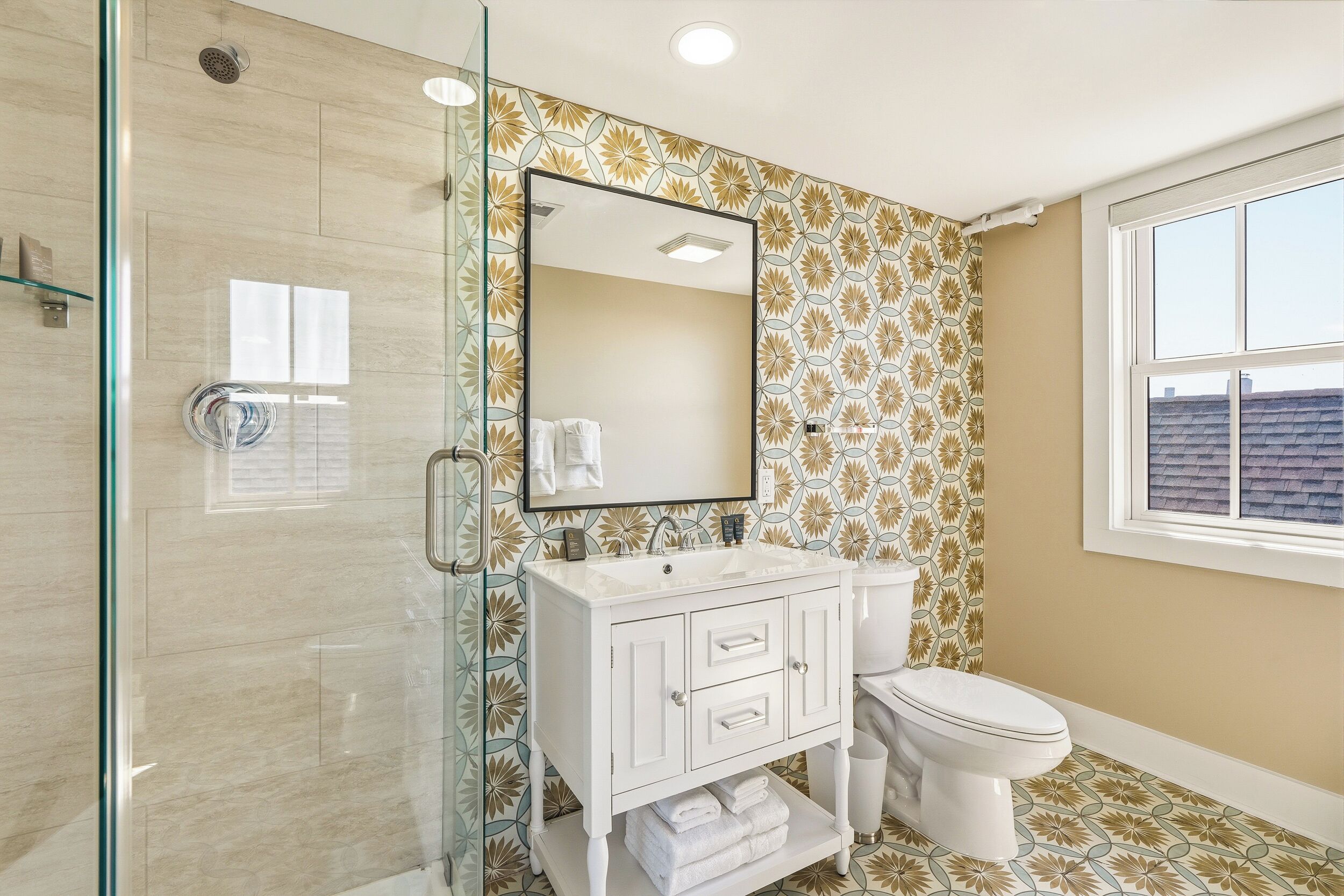 A bathroom with a glass shower enclosure, a white vanity with a mirror, and a toilet.