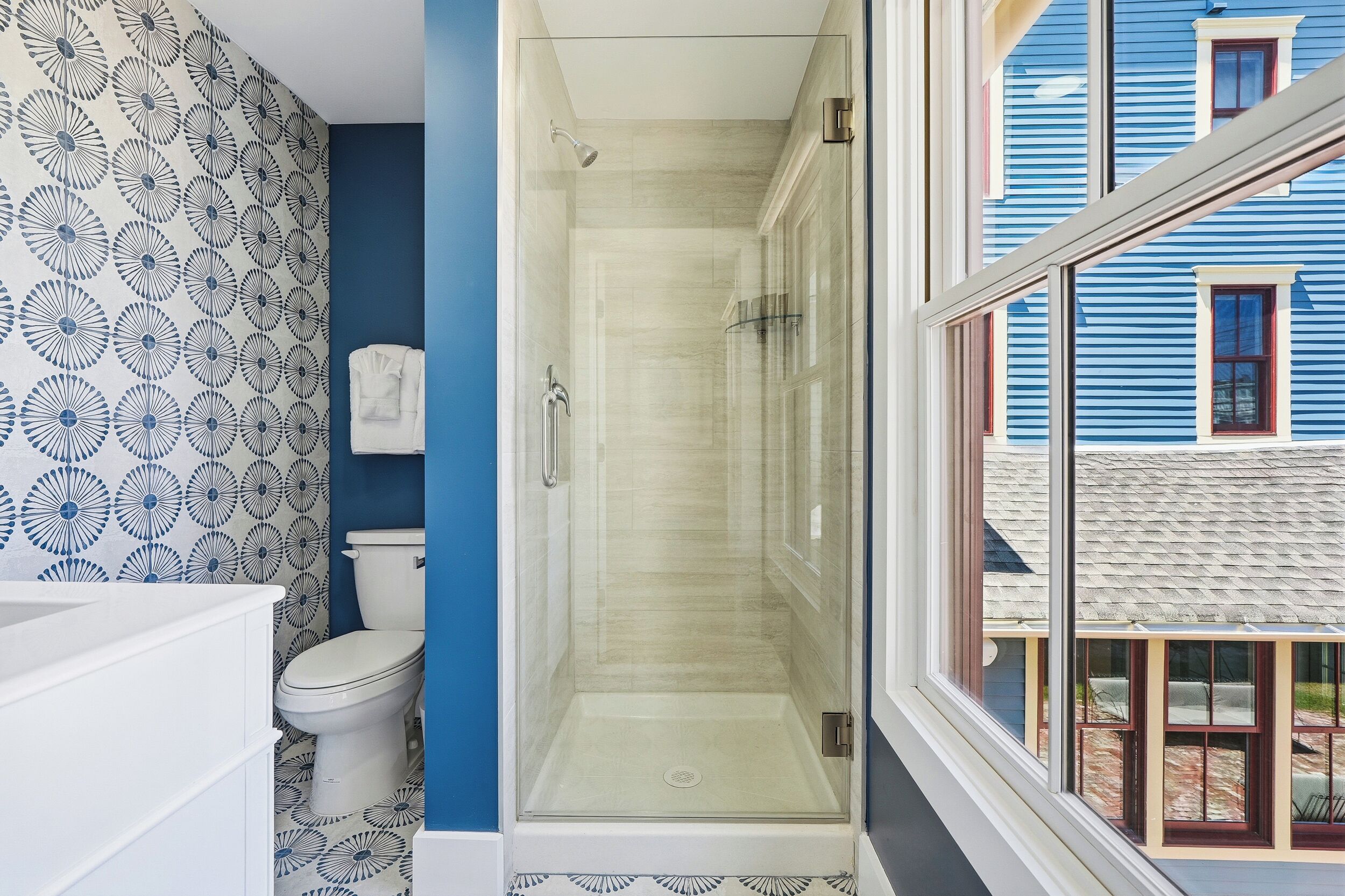 A bathroom with a shower, toilet, and a window with a view of a blue building.