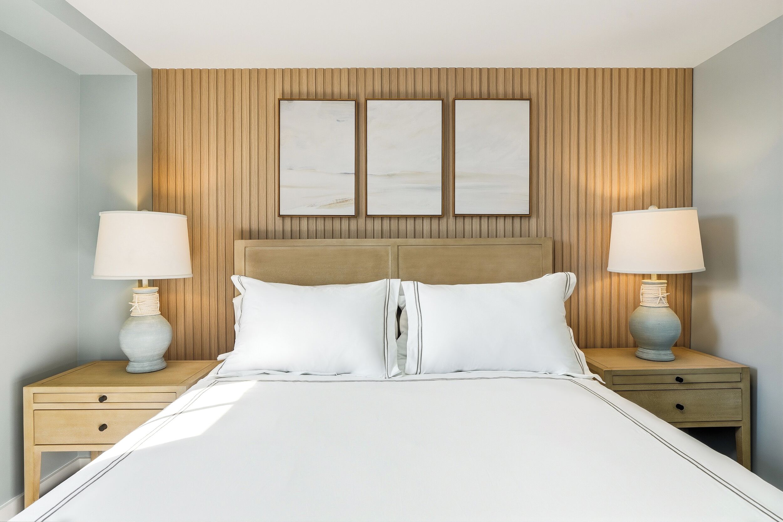 A bed with a headboard, two bedside tables with lamps, and three wall-mounted artworks.