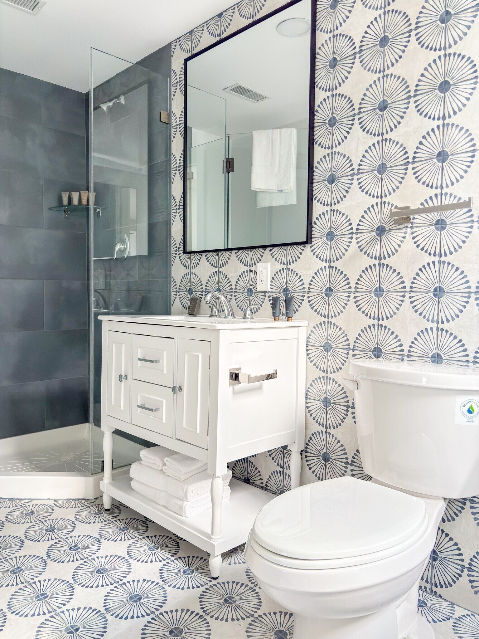 Een badkamer met een douchecabine van glas, een wit wastafelmeubel met lades, een toilet en een spiegel boven het meubel.
