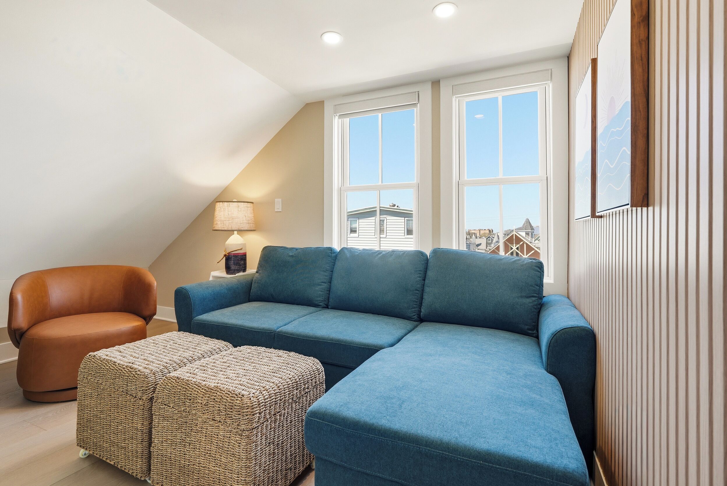 A modern living room with a sectional sofa, a leather armchair, and a woven ottoman.