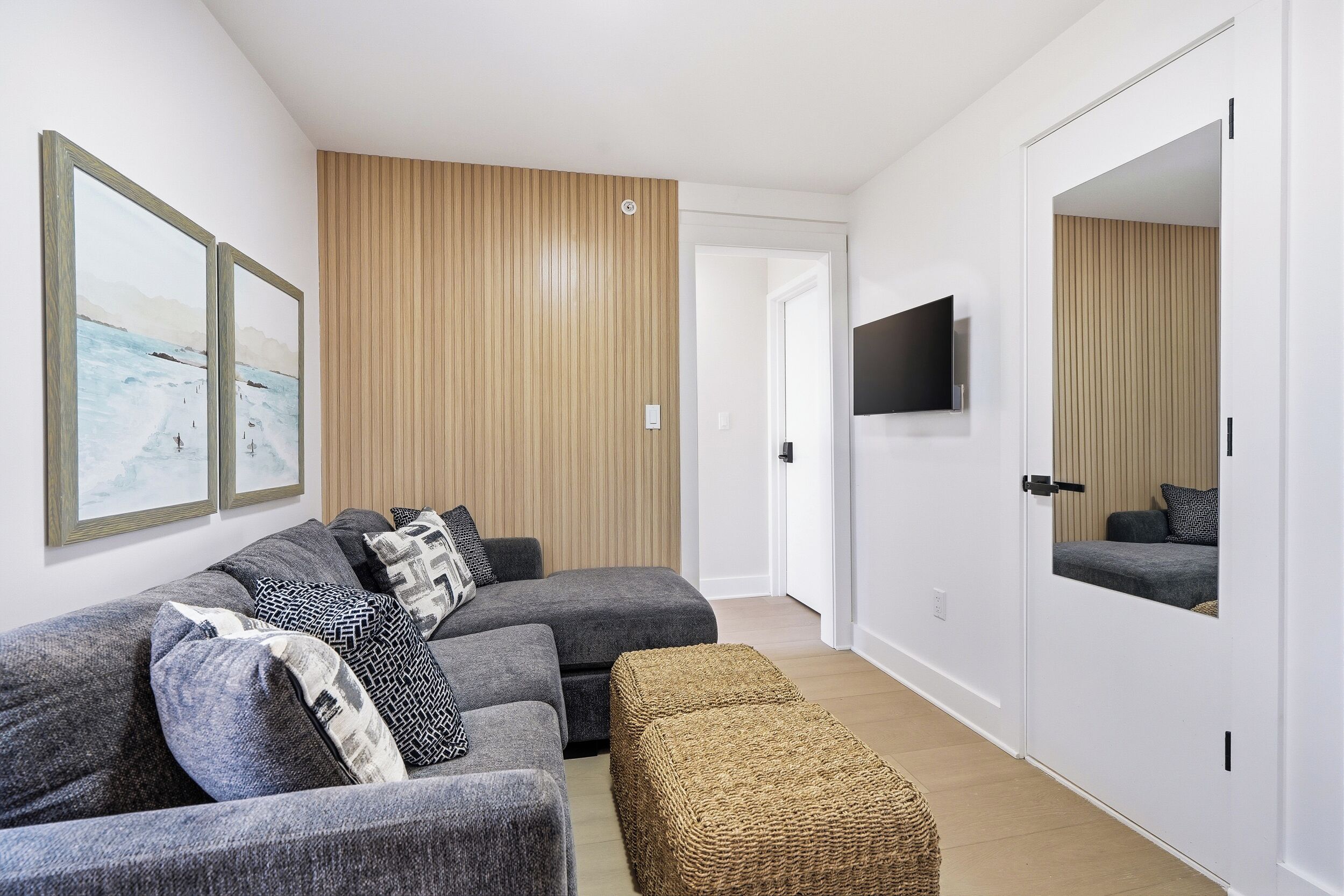 A modern living room with a sectional sofa, a flat-screen TV, and a large mirror.