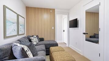 A modern living room with a sectional sofa, a flat-screen TV, and a large mirror.