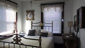 A bedroom with a bed, a bedside table, a lamp, and a mirror. - The Historic Argo Hotel (Crofton)