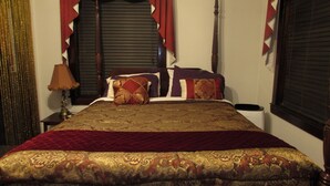 A neatly made bed with a patterned bedspread and pillows, a bedside lamp, and a window with closed blinds. - The Historic Argo Hotel (Crofton)