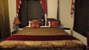 A neatly made bed with a patterned bedspread and pillows, a bedside lamp, and a window with closed blinds.
