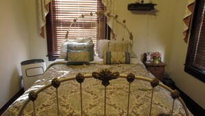 A bedroom with a bed, bedside table, lamp, and a window with blinds. - The Historic Argo Hotel (Crofton)