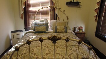 A bedroom with a bed, bedside table, lamp, and a window with blinds.