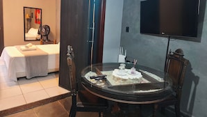 Ein Hotelzimmer mit Bett, Esstisch mit Kuchen, Fernseher und Ventilator.