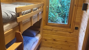 Habitación de cabaña de madera con literas, una ventana con vistas a la vegetación y un enchufe pequeño en la pared.