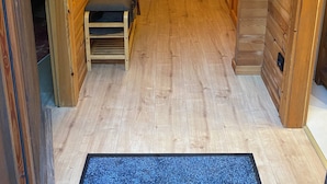 Un estrecho pasillo de madera con un banco, una lámpara de pared y una puerta que da a otra habitación.