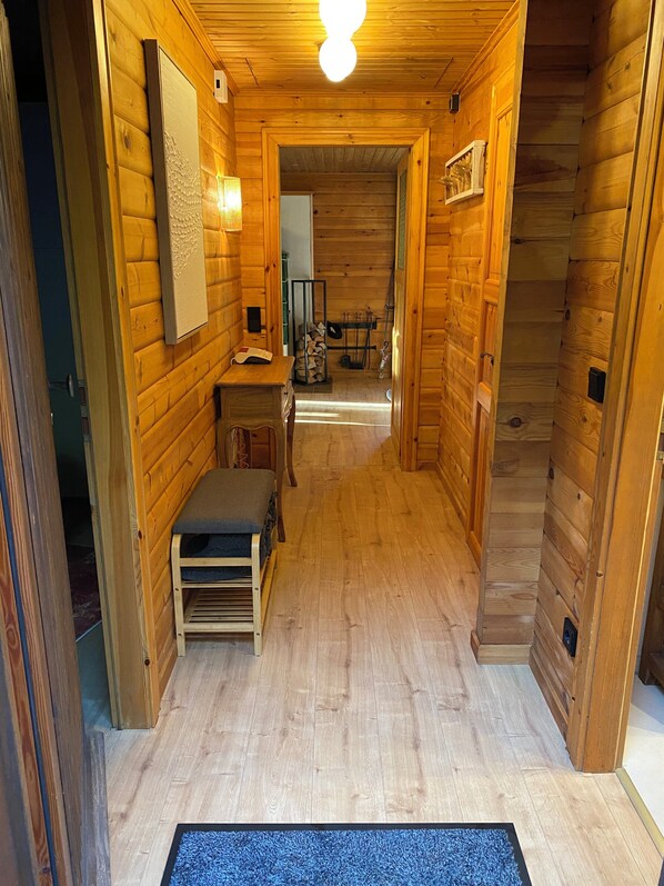 A narrow wooden hallway with a bench, a wall-mounted light fixture, and a door leading to another room.