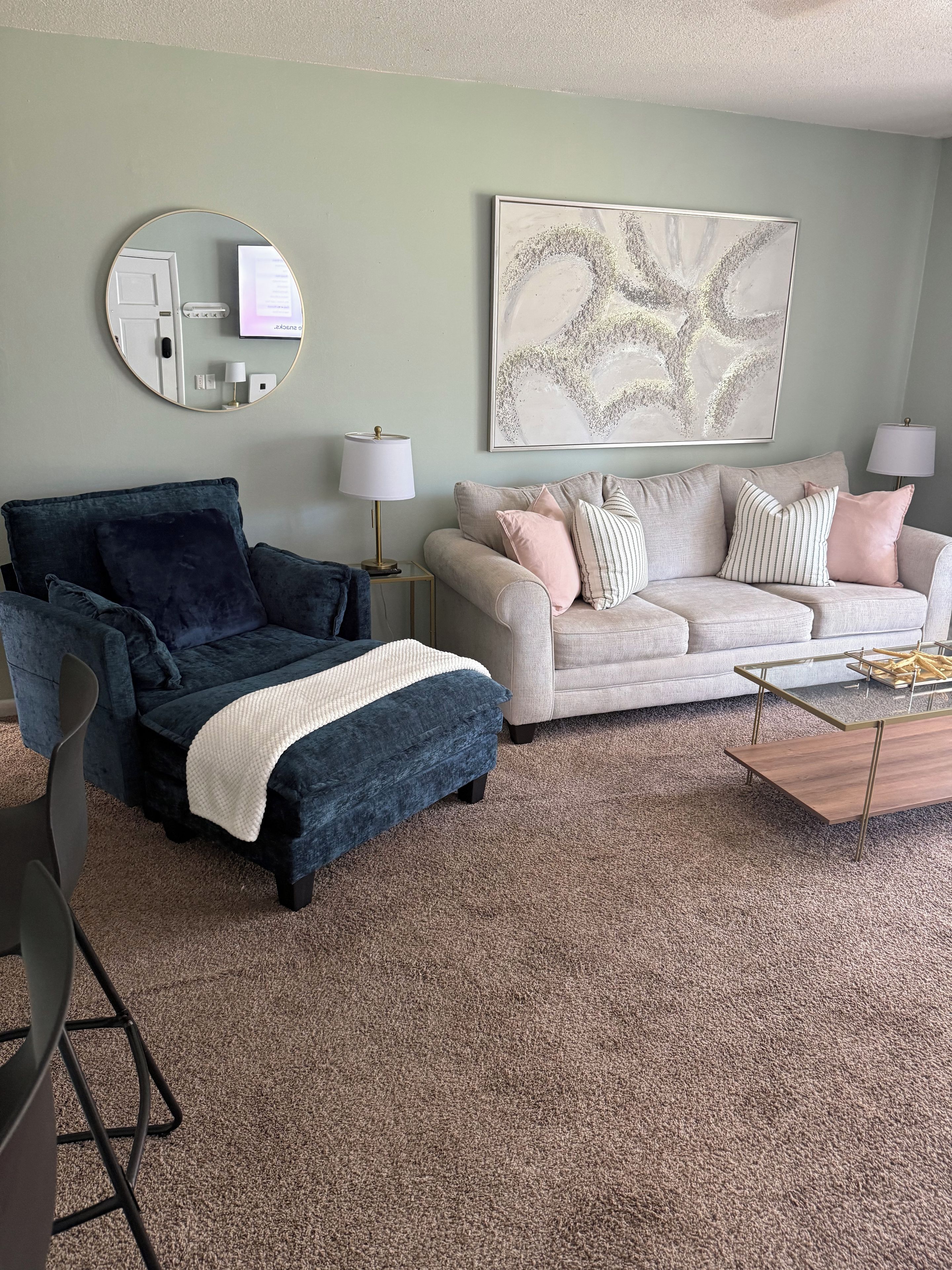 A living room with a blue armchair, a beige sofa, a coffee table, and a carpeted floor.