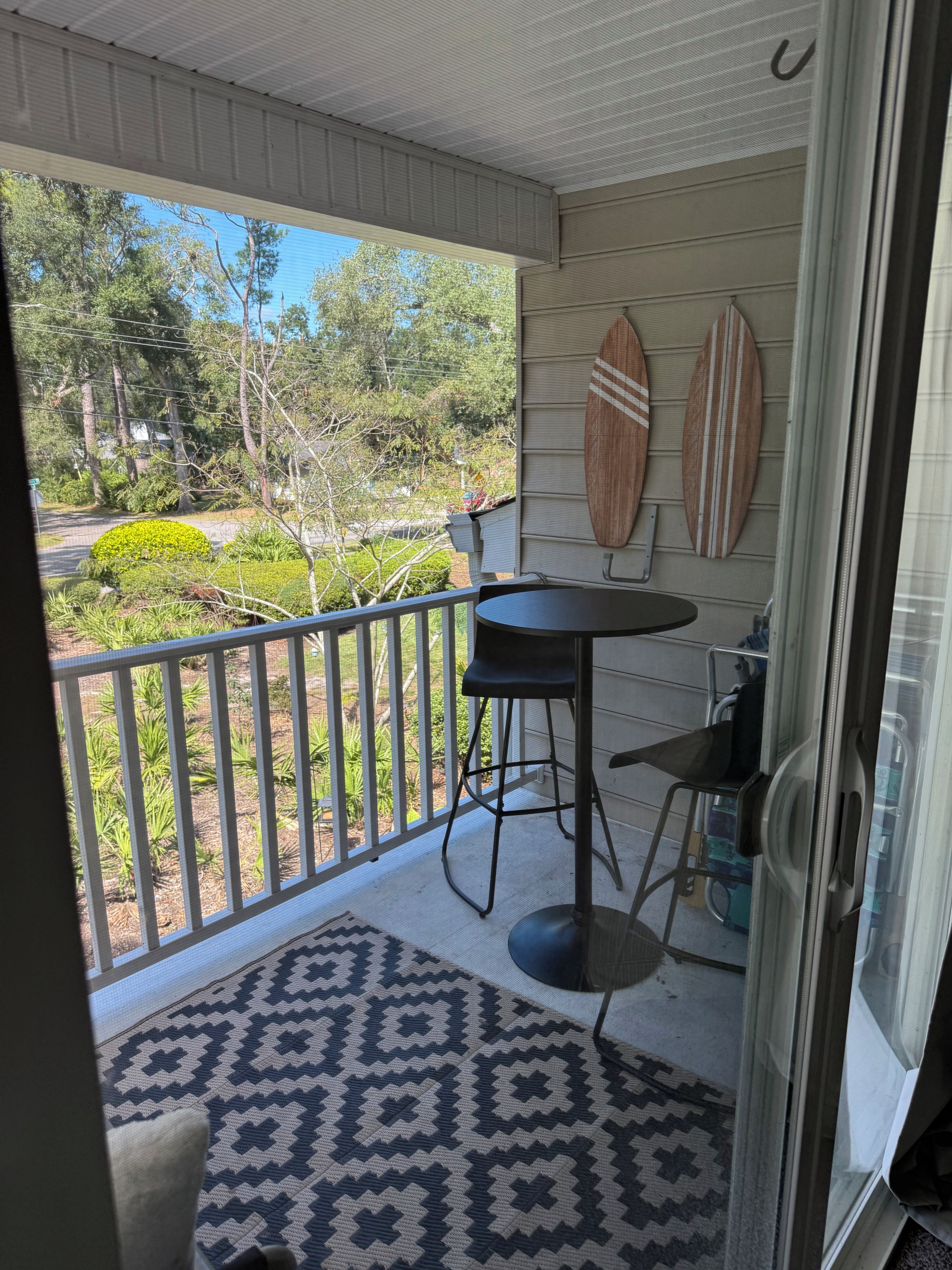 A covered balcony with a patterned rug, a table, and two surfboards mounted on the wall.