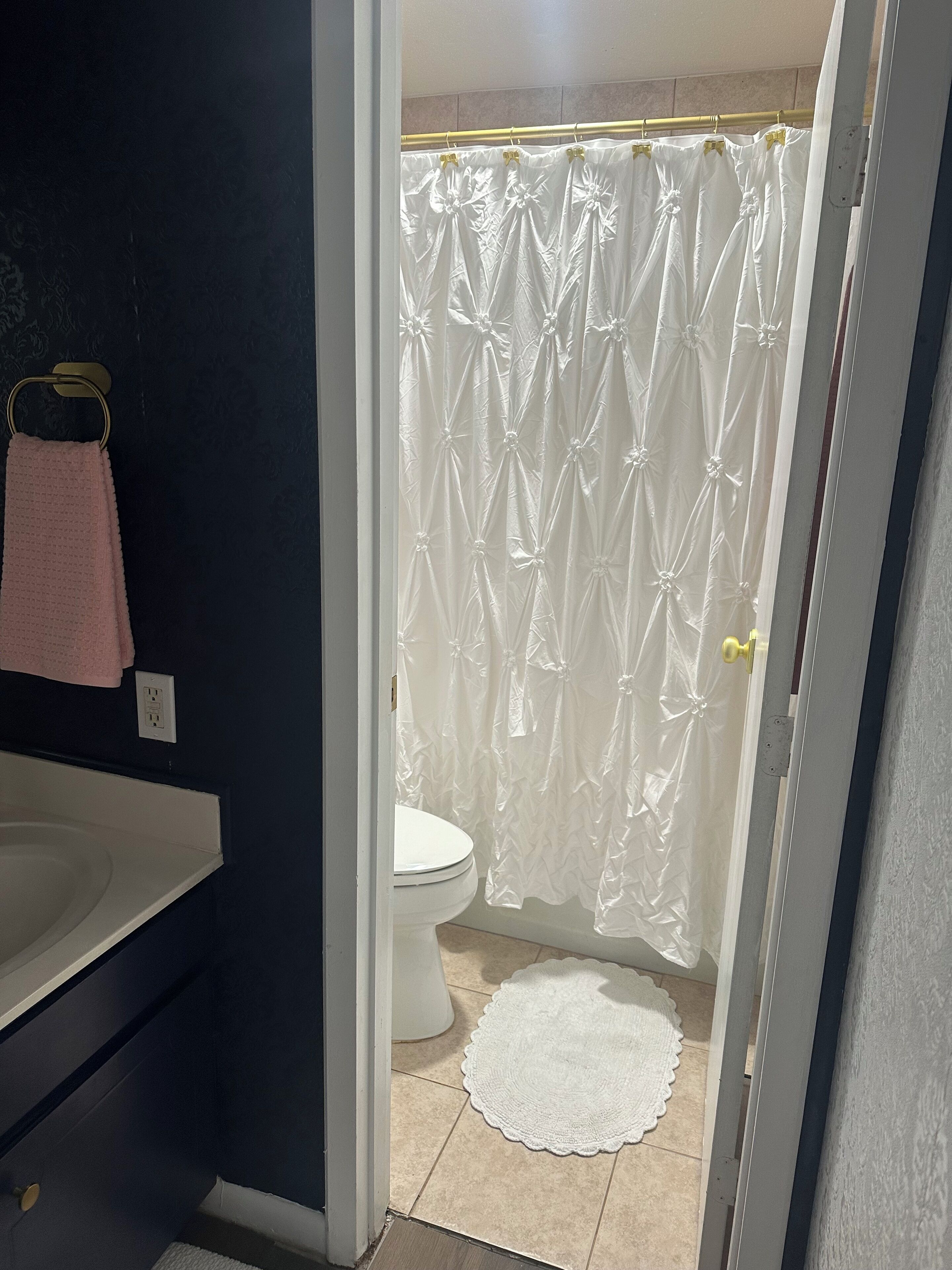Un baño con inodoro y lavamanos blancos, y cortina de ducha con estampado floral.