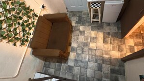 Een kamer met een bruine bank, een kleine tafel, een koelkast en een trap.